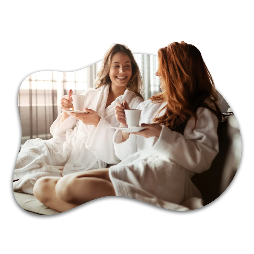 Two friends relaxing in white spa robes enjoying tea together